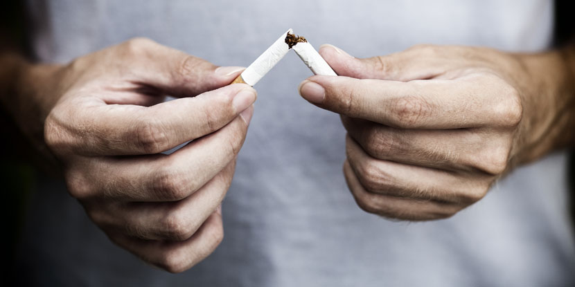 A man's hands are seen in close-up, breaking a cigarette into two pieces.