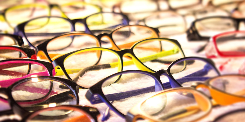 Close-up of many pairs of eyeglasses arranged on a lighted table.