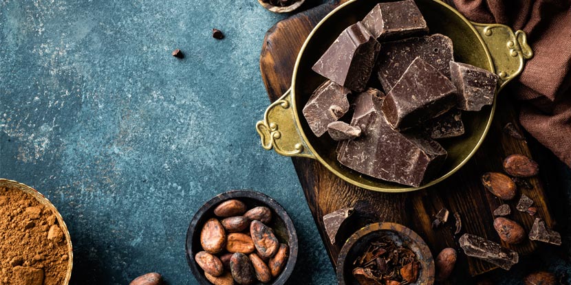 Una taza para medir llena de chocolate oscuro, granos de cacao y chocolate el polvo vistos desde arriba sobre un mostrador.