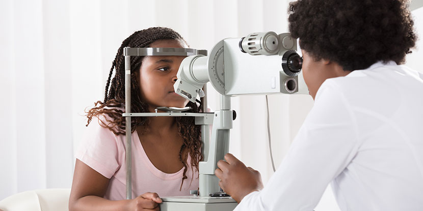 A teenage girl receives a slit lamp eye exam from an ophthalmologist.