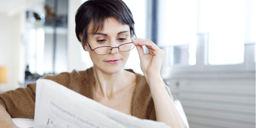 An older woman with newspaper and reading glasses