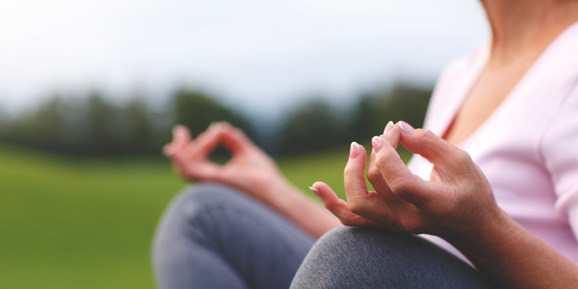 Acercamiento de las manos de una mujer en posición de meditación, al aire libre.