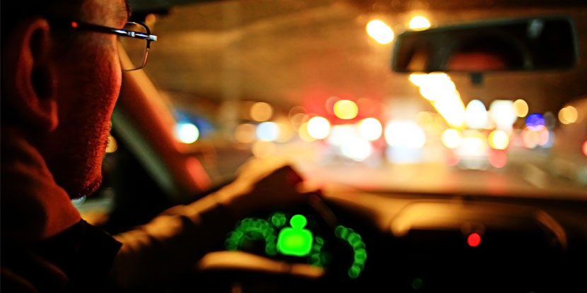 Vista del interior de un automóvil en la noche, con el conductor y, adelante, las luces traseras del tráfico.