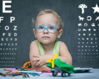 Child in glasses sitting at desk in front of blackboard