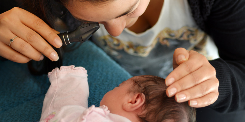A woman examines an infant's eye with a handheld ophthalmoscope.