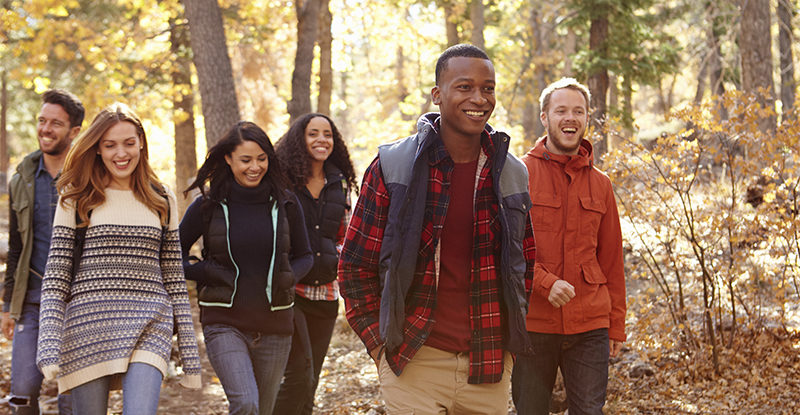 A group of smiling young adults walking in the woods and wearing fall clothing