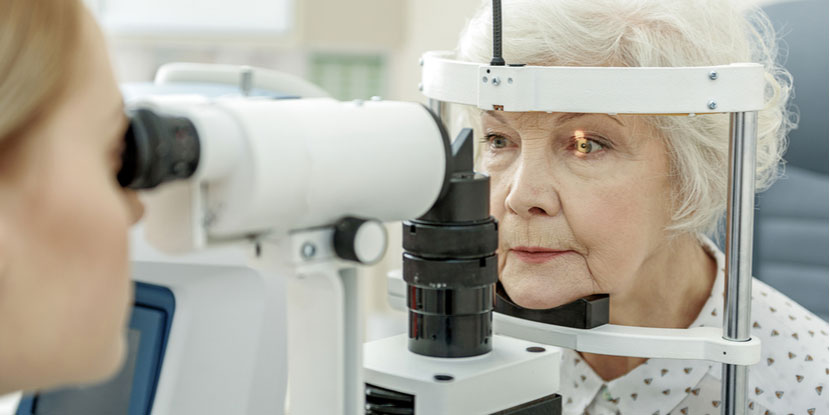 Foto de un oftalmólogo que usa una lámpara de hendidura para mirar los ojos de una mujer mayor.
