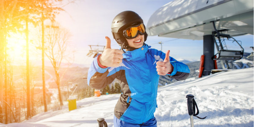 Joven sonriente en la estación de esquí en un día soleado sonriendo a la cámara antes de ir a esquiar