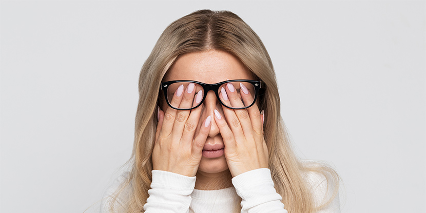 A woman has pushed her glasses up and is rubbing her eyes