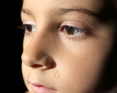 Closeup photo of a child with a tear running down his cheek, against a black studio background.