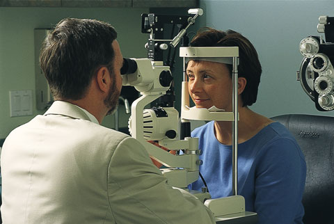 A woman is examined by an ophthalmologist using a slit lamp, in a doctor's office.
