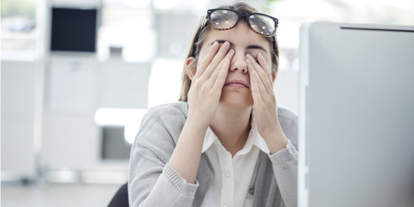 Una mujer en su escritorio, trabajando en su computadora, se frota los ojos para aliviar la fatiga ocular