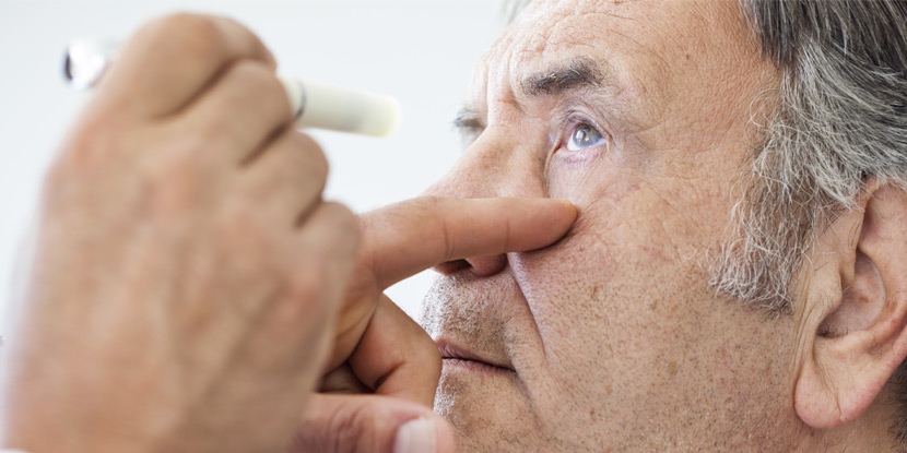 An older man has a penlight shone into his eye to check vision