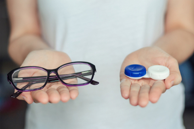 A woman is holding a pair of glasses and a contact lens case