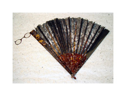 A folding hand fan with a small pair of eyeglasses attached to the end of one handle. The fan is black and red lace and the handles are tortoise shell. The glasses are small with brown frames.