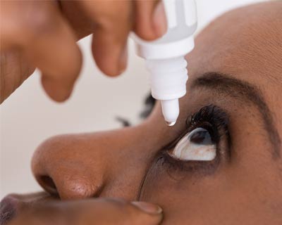 Closeup of a woman putting in (instilling) eye drops into her eye.
