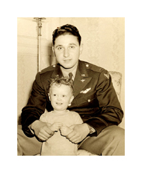 A black and white photograph of a man in military uniform holding a young child. He is a young, white man with dark hair and a dark uniform, and he crouches behind a standing little boy with curly hair.