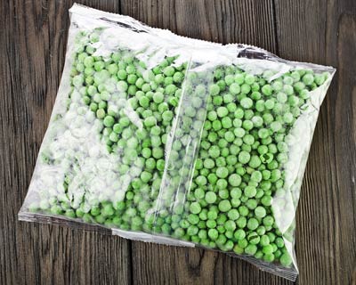 A clear plastic bag of frozen peas sits on a wooden surface.