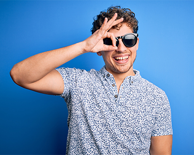 Smiling young man wearing sunglasses looks through fingers