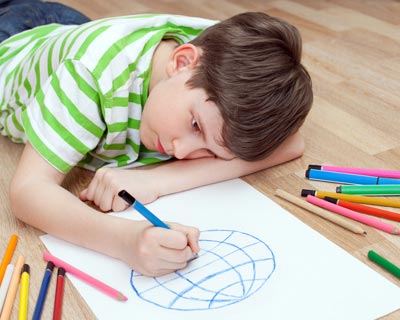 Photograph of a boy on the floor drawing a picture