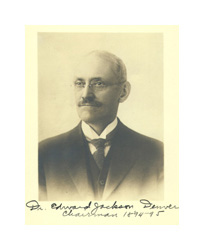 An autographed sepia-toned photograph of a man with a mustache. He is bald with a dark mustache, and he wears eyeglasses and a dark suit. A black ink signature across the bottom of the photo reads: Dr. Edward Jackson, Denver.