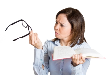 Woman looking at glasses and book.
