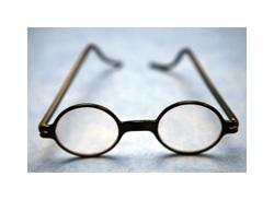 A brown pair of eyeglass with circular lenses and bent earpiece ends sits on a white surface.