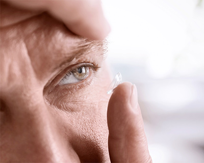 A closeup of a man's face and hand. He has a contact lens on his finger and is about to place the contact on his eye.