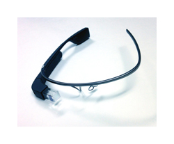 A pair of black, computerized eye glasses. They are made up of a black plastic band, small clear lenses, and a small camera held out in front of the lenses.