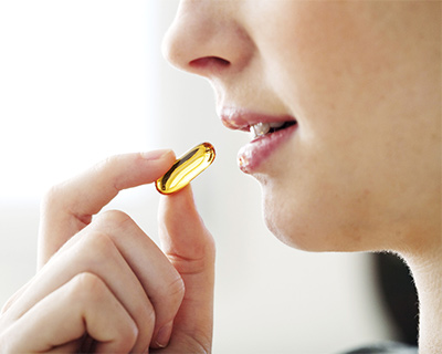 A woman is holding a dietary supplement pill and is about to put it in her mouth.