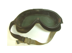 A pair of plastic over-the-eye goggles with an elastic strap sit on a white background. Both the goggles and the strap are an olive, Army green.