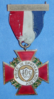 A ribbon holding an award medal. The ribbon has red, white and blue, stripes, and it holds a red, cross-shaped medal. The medal has green laurels around the cross-shape, and the center is white. The center of the medal reads: AOS Prize in Ophthalmology.