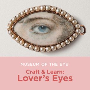 An almond shaped painting of a woman's eye, eyebrow, and a wisp of hair. The woman has light skin, blue eyes, and brown hair, and the painting is bordered with white pearls and gold metal. Underneath, there is a pink bar with white and red lettering that reads: Museum of the Eye Craft & Learn: Lover's Eyes.