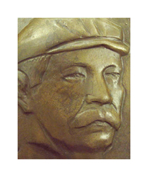A bronze-colored plaque with a man's face. The man is wearing a soft brimmed hat, and has a thick mustache. He is turned lightly in profile towards the right.