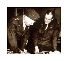 Two men in military uniforms examine a book in front of them. Both are middle aged white men wearing dark uniforms. The man in the foreground wears a cap, and the other man has dark hair and a mustache.