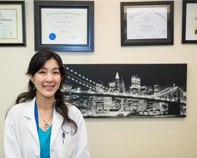 Dr. Song stands with her diplomas in her office.