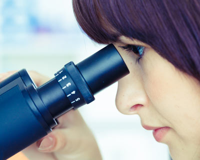 Fotografía de una mujer que mira en microscopio