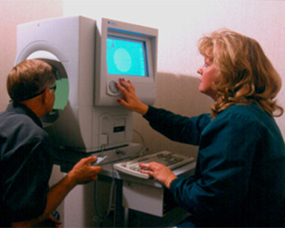 A patient sits at a perimeter machine taking a visual field exam.